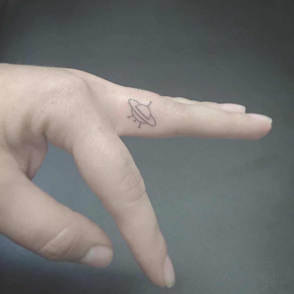 Small UFO tattoo on the left middle finger