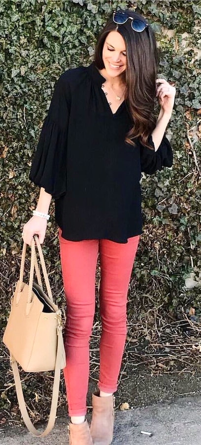 Black long-sleeve top and red skinny jeans holding brown two-way handbag with sunglasses.