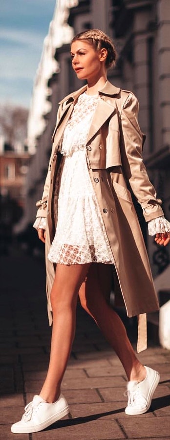 White lace mini dress with beige coat and pair of white low-top sneakers.