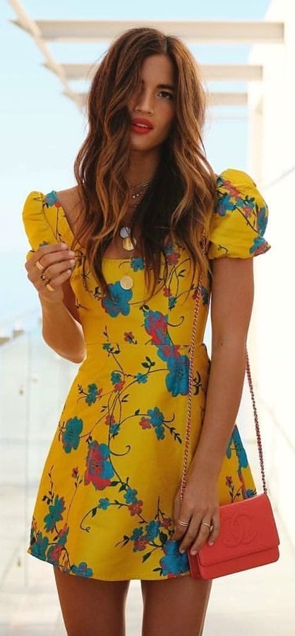 Woman in yellow and blue floral puff-sleeved dress carrying pink Gucci bag.