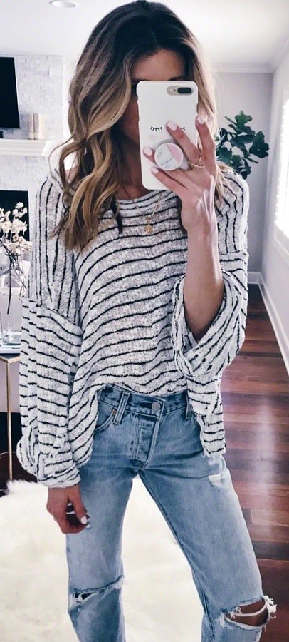 Woman wearing gray sweater and denim jeans holding white smartphone.