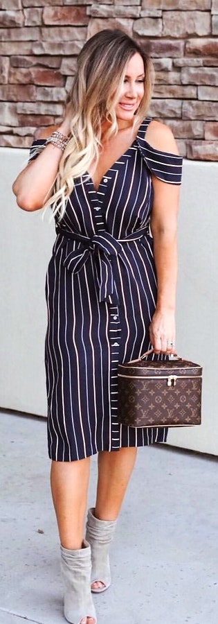 Black and white striped cold-shoulder midi dress holding monogrammed LV handbag.