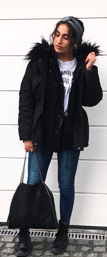 Black full-zip parka jacket and blue jeans holding purse.