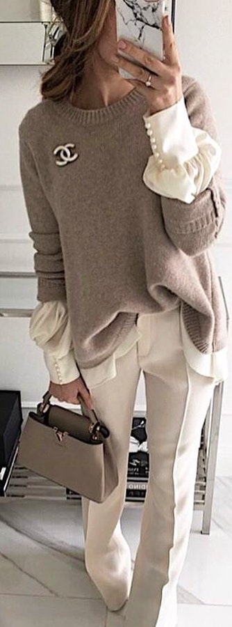 Gray Chanel sweater and white dress pants holding gray leather handbag.