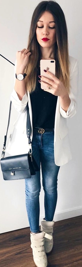 White blazer, blue denim jeans, white shoes with black handbag.