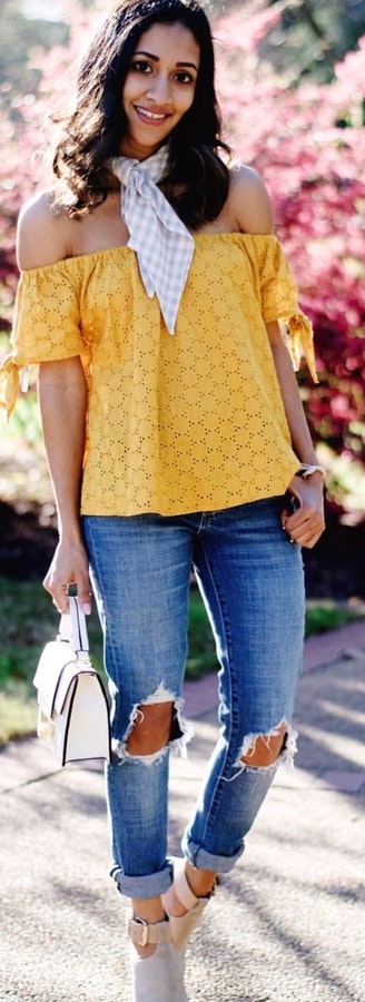 Yellow off-shoulder shirt, distressed blue-washed boyfriend jeans, and pair of gray booties outfit.