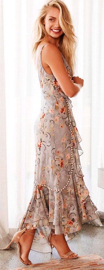 Grey beige and red floral sleeveless dress stands near white chiffon curtain.