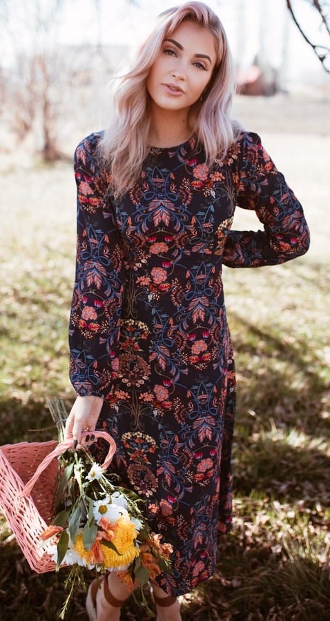 Woman in blue and red floral long sleeve dress holding pink wicker basket.