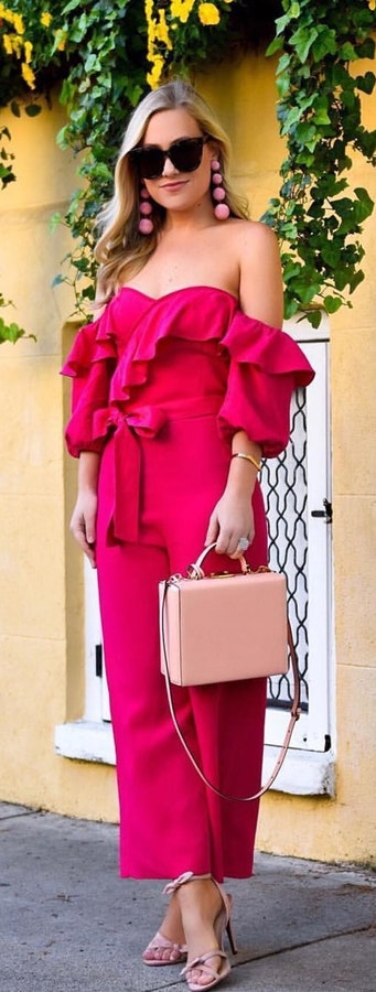 Woman in pink off shoulder dress standing holding pink leather 2 way bag.