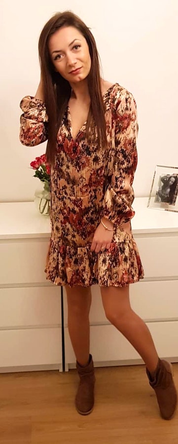 Woman wearing brown and red floral v neck long sleeved mini dress standing beside IKEA Malm dresser.
