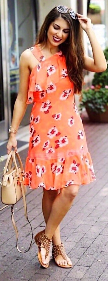 Woman wearing orange floral sleeveless dress with 2 way bag and sunglasses.