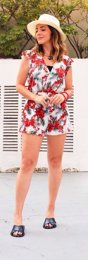 Woman wearing pink and multicolored floral v neck romper and brown sun hat.