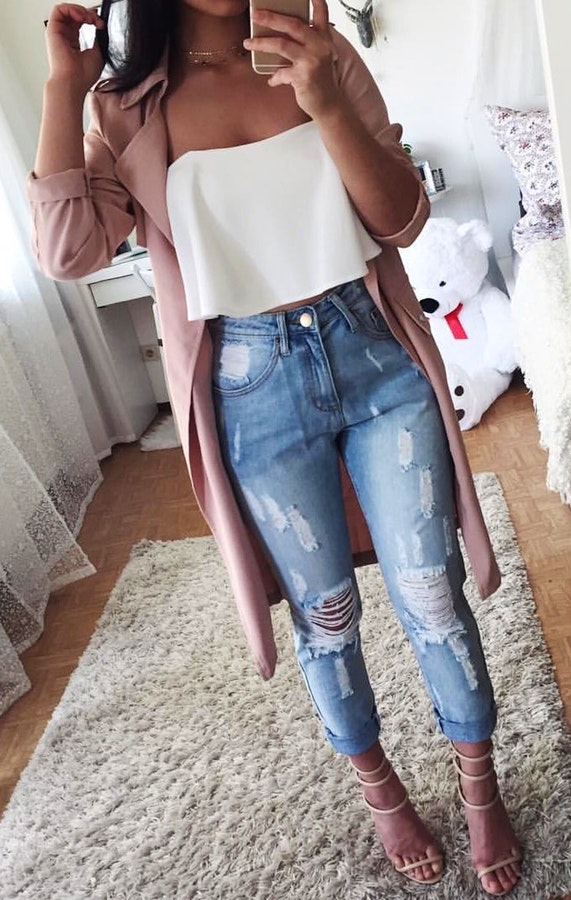 Women's white tube top and blue distress jeans with peach coat.
