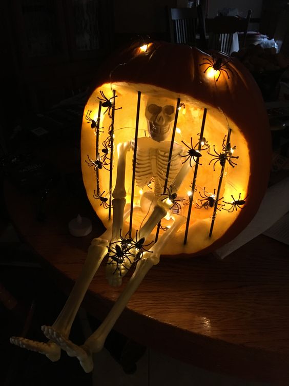 Skeleton in jail carved pumpkin lit with battery operated LED spider lights. Painted skewers black for prison bars.